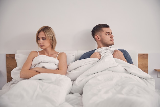 Cute blond woman and brunette male lying in bed and looking to different sides