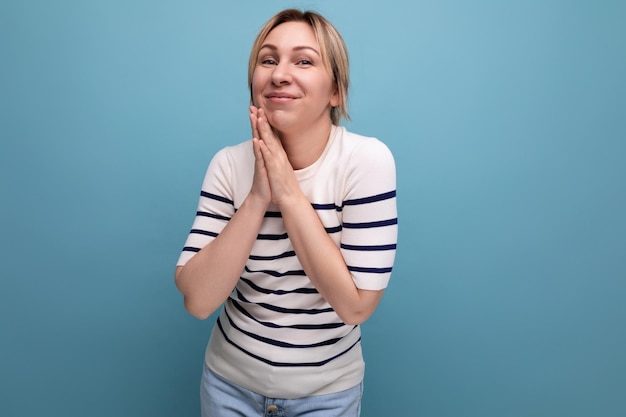 Cute blond young woman in a striped sweater on a blue background with copy space