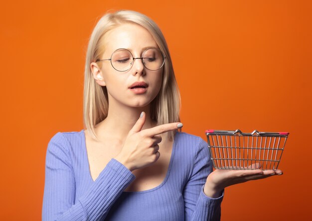 Photo cute blonde in blue blouse with shopping basket on an exuberant orange color background