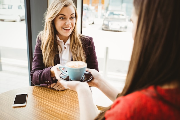 Cute blonde girl having a coffee served by her friend in a coffee shop