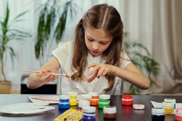 Cute blonde girl painting with acrylic paint in art studio class.