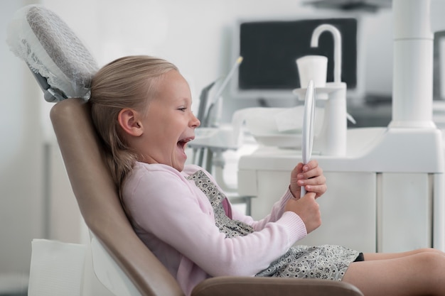 Cute blonde girl sitting in the chair at the dentists