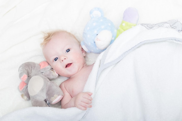 Cute blonde little baby boy with blue eyes with his favorite plush teddy bear and elephant.