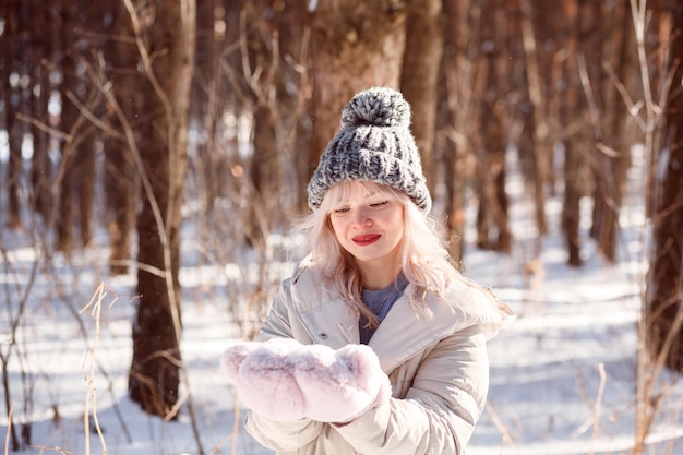 Cute blonde woman in knitted cap with bombon and warm gloves spending time outdoors in winter