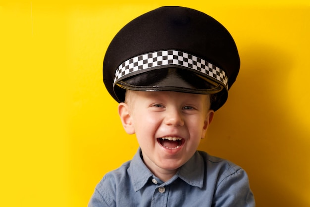 Cute boy in a cap of a policeman laughs on a yellow background