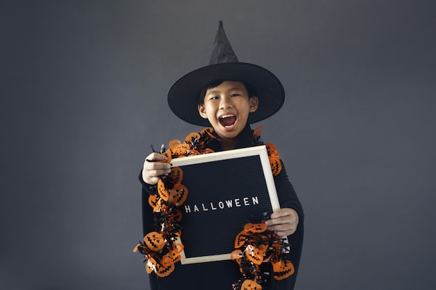 Photo cute boy celebrating halloween by wearing witch costume and holding halloween decoration accessories