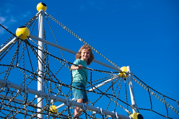 Cute boy climbing net in the park and having fun on the playground