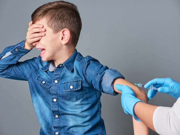 Cute boy crying while being vaccinates isolated on gray