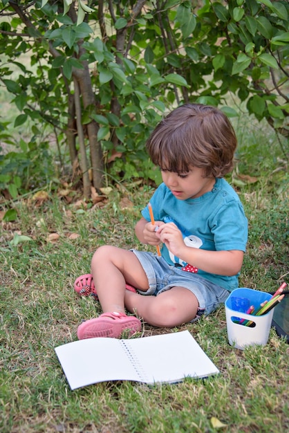 Cute boy doing homework laying on grass Child reading a book in the summer park Concept of kids learning study outdoors in the park