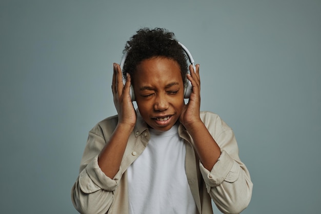 Cute boy of generation alpha touching headphones on his head while keeping eyes closed and enjoying