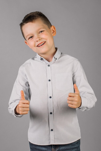 A cute boy on a gray background points his hand to the side looks and smiles at people with sincere emotions the concept of a child's lifestyle