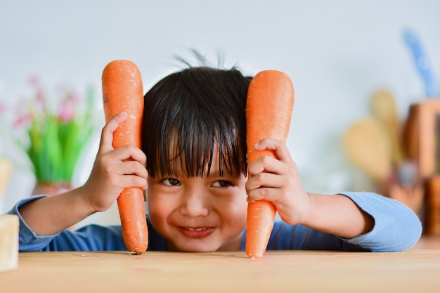 Cute boy holding a carrot. And make a Looks crafty in the kitchen.