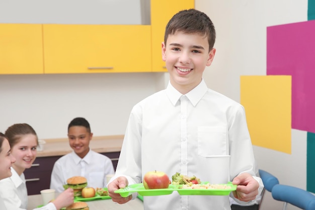 Cute boy holding tray with delicious food in school canteen