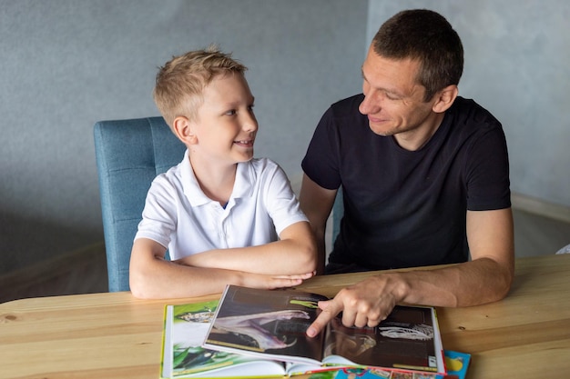 A cute boy is sitting at the table with his dad and watching a book about snakes