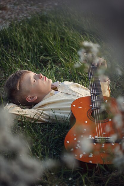 Photo cute boy lies on the grass with a guitar on sunset