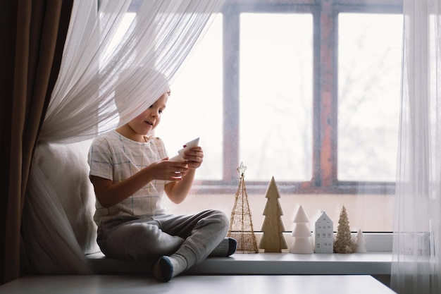 Cute boy playing with kitten sitting on the windowsill near the window cozy home