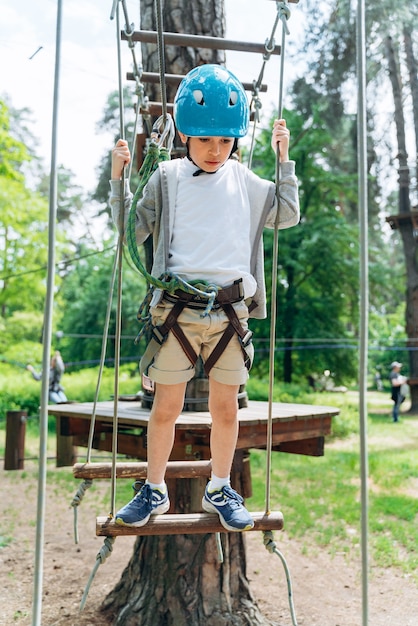 Cute boy in a protective helmet, an insurer passes obstacles in a rope park. The boy looks down