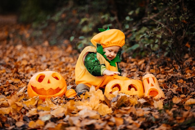 Cute boy in pumpkin costume among carved pumpkins