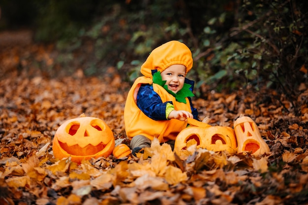 Cute boy in pumpkin costume among carved pumpkins