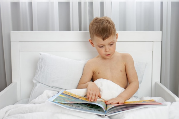 Cute boy reading a book in a white bed