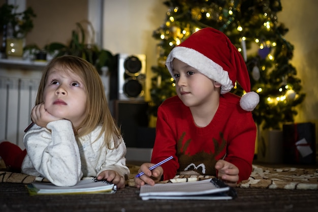 Cute boy in red sweater and red santa hat writes a letter to Santa