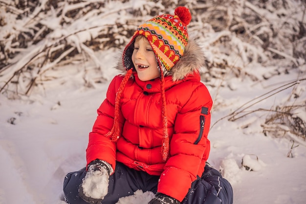 Cute boy in red winter clothes builds a snowman winter fun outdoor concept