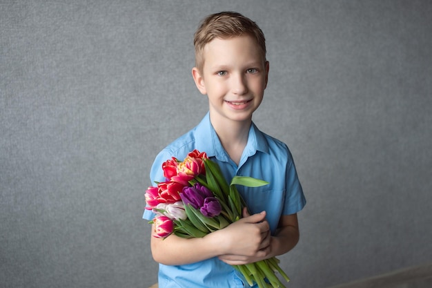 A cute boy in a shirt holds a colorful bouquet of tulips in his hands Space for text