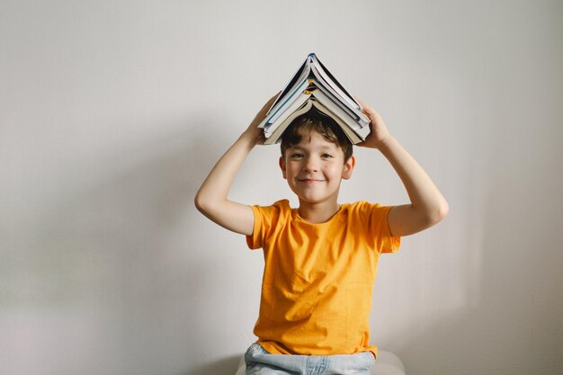 A cute boy wearing an orange tshirt is sitting on a soft ottoman reading a book