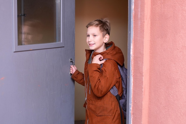 Cute boy with a backpack opens the door