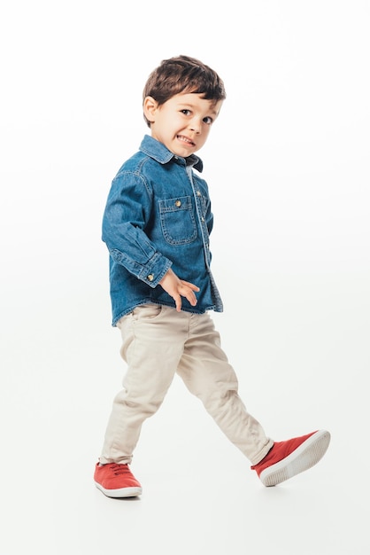 Cute boy with face expression in denim shirt walking on white background