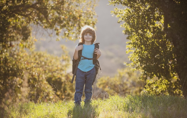 Cute boy with hiking equipment in the mountains. Child hiker with backpack hike in hills background.