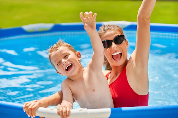 cute boy with his mother playing in a pool of water during the summer