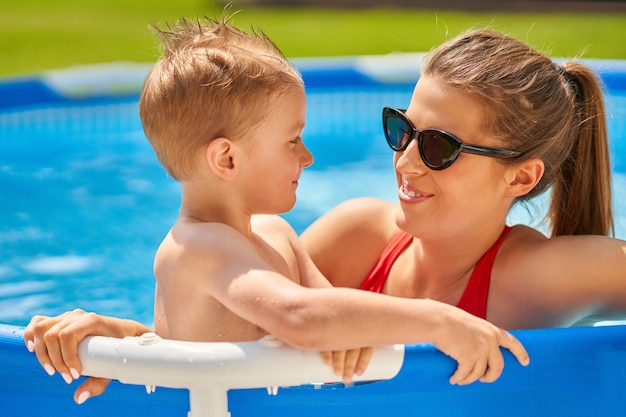 cute boy with his mother playing in a pool of water during the summer