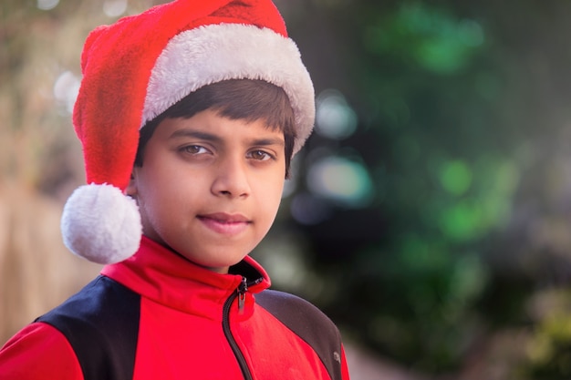 A cute Boy with Santa cap red tshirt smiling happily and looking at the camera