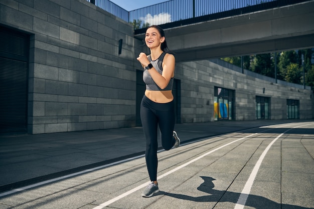 Cute brunette woman expressing positivity while running on the sidewalk, enjoying her active lifestyle