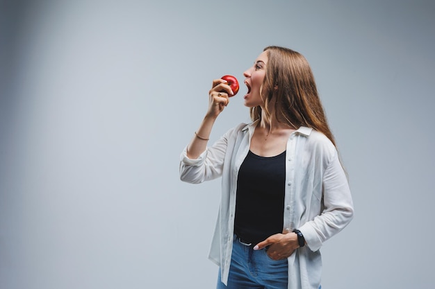 Cute brunette woman in white shirt holding red apple in hand standing on isolated white background dietetics and nutrition Healthy food