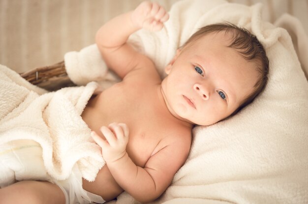 Cute caucasian baby boy lying under blanket on bed