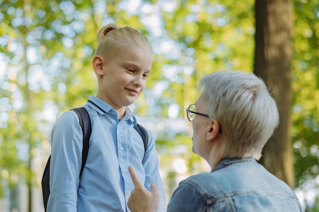 Cute caucasian blonde boy with ponytail going to school Mother having a conversation with child