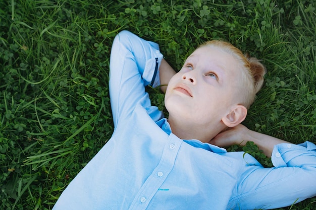 Cute caucasian blonde boy with ponytail having rest on grass