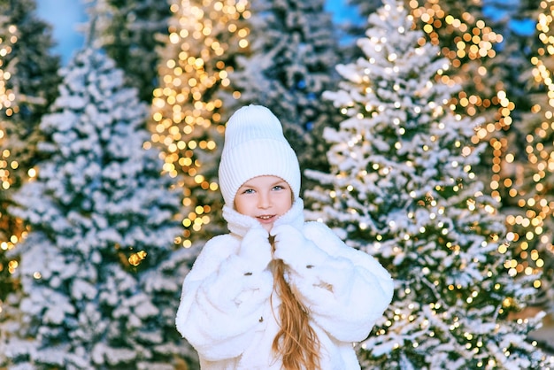 cute caucasian blonde girl in white eco fur coat, hat and gloves walking in the winter christmas