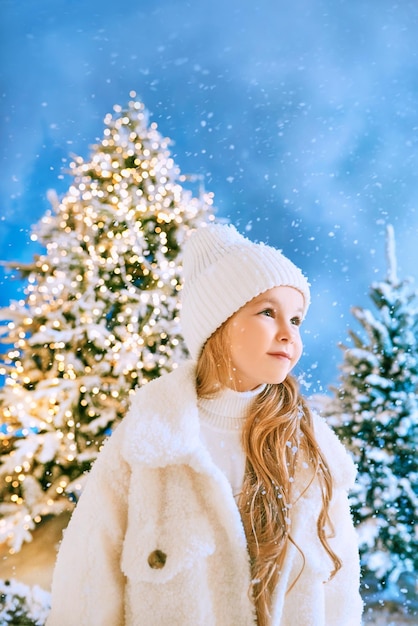 cute caucasian blonde girl in white eco fur coat, hat and gloves walking in the winter christmas