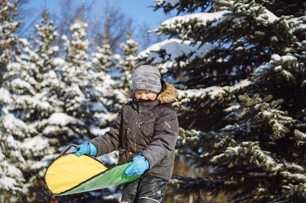 Cute caucasian boy holding a snow saucer to slide from hill in winter park. High quality photo