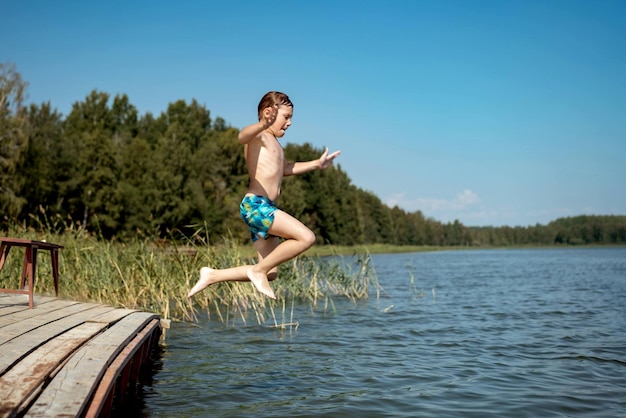 Cute caucasian boy jumping from wooden pier diving into lake in countryside