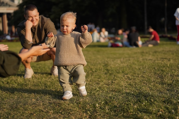 cute caucasian boy learning to walk on lawn in park his mother opening wide arms to catch him