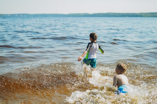 Cute caucasian boy running into water with splashes and laughter Vacation on seaside Happy childhood