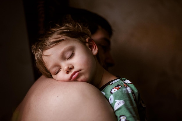 Cute caucasian boy sleeping putting head on father's shoulder Fatherhood concept Parent care support and safety