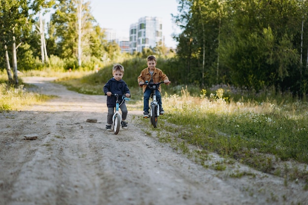 Cute caucasian boys brothers are cycling together in countryside in summer time Little one is riding runbike elder one riding bicycle Image with selective focus