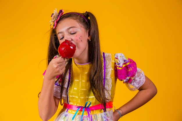 Cute caucasian girl in typical festa junina outfit eating apple with caramel