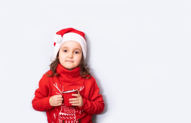 Cute caucasian kid girl in red Santa's hat holding red mug or cup empty copy space for design or text Banner Christmas mockup template