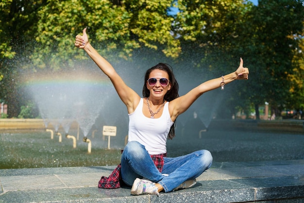 Cute caucasian woman sits by fountain in park on sunny day enjoys the coolness